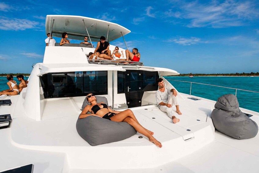 A yacht with people lounging on deck chairs and bean bags, surrounded by clear blue water and a distant shoreline. 5