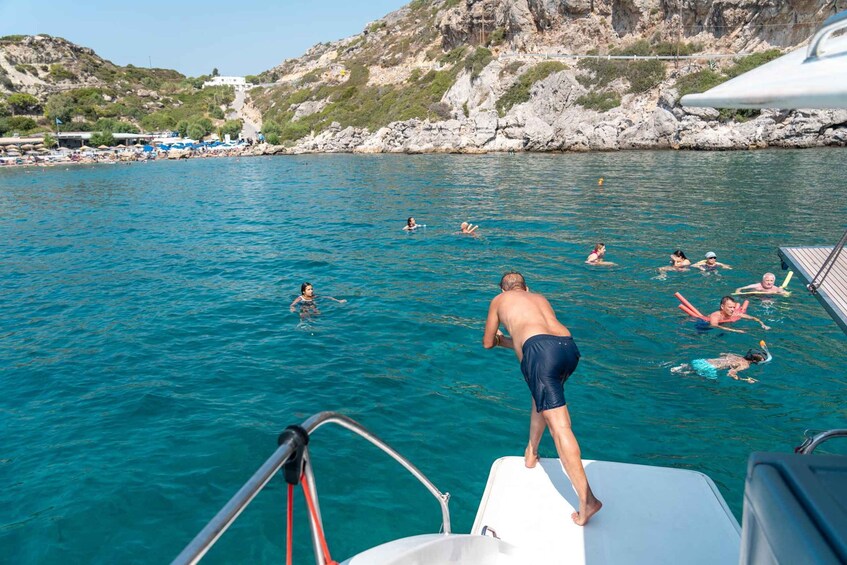 A group of people swimming and floating in a clear blue sea with rocky hills in the background. 4