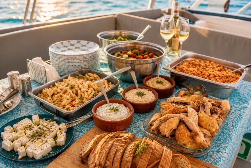 A buffet table with various dishes, including pasta, chicken, and dips, set on a boat with a view of the sea. 3