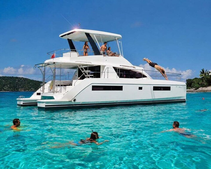 A white yacht with people swimming in the water around it. 1