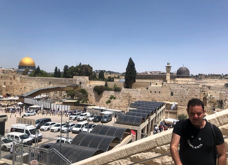 A man standing in front of a parking area with solar panels, overlooking the Dome of the Rock and the Western Wall. 1