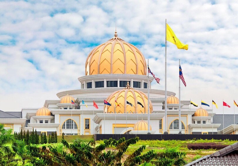 A large building with a prominent golden dome, multiple flags, and a landscaped foreground. 3