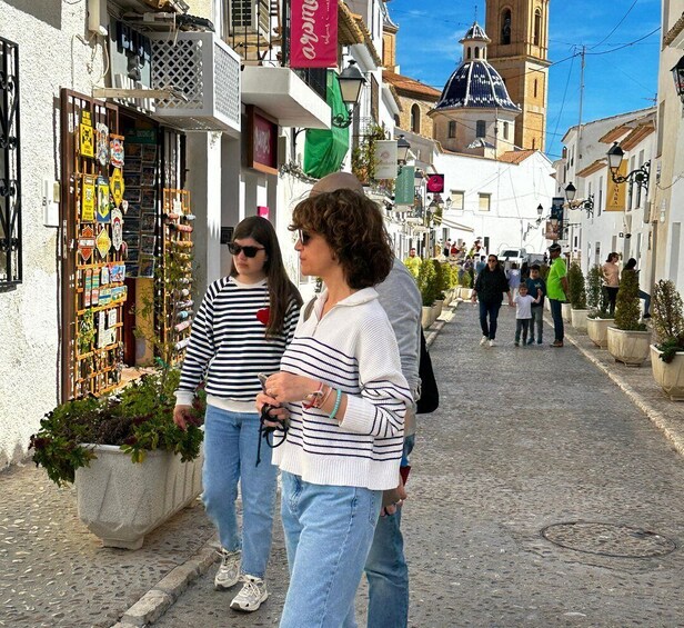 A cobblestone street lined with shops and a church tower in the background. 4