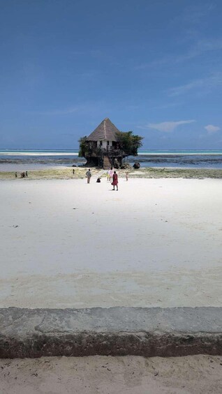 A beach with a thatched-roof hut and people walking on the sand. 2