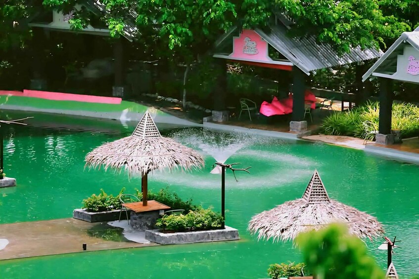 A tranquil pool with thatched umbrellas, a small island with plants, and a gazebo in the background. 2