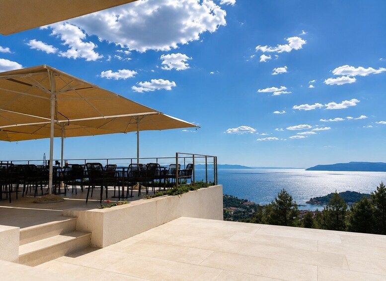An outdoor seating area with chairs and a table under a canopy, overlooking a scenic view of a body of water and distant hills. 1