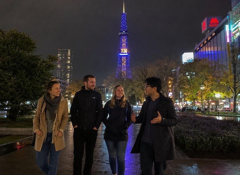 A group of people walking on a city street at night with illuminated buildings and a prominent tower in the background. 2