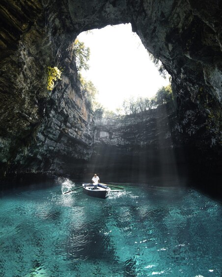A person in a boat inside a cave with clear water and sunlight streaming through an opening. 2