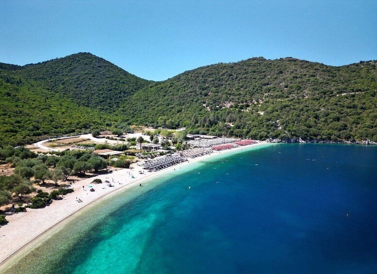 A coastal beach with clear turquoise waters, a sandy shore, and lush green hills in the background. 1