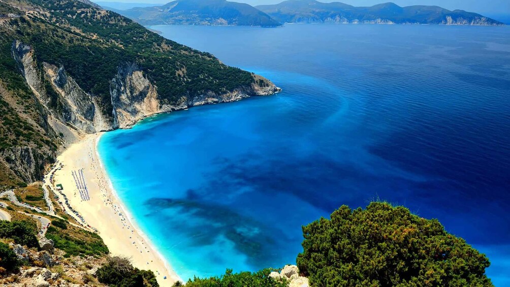 A coastal landscape with a beach, clear blue waters, and a mountainous backdrop. 3