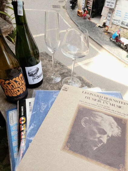 A bottle of wine, two empty wine glasses, a newspaper, and a blue envelope on a table. 5