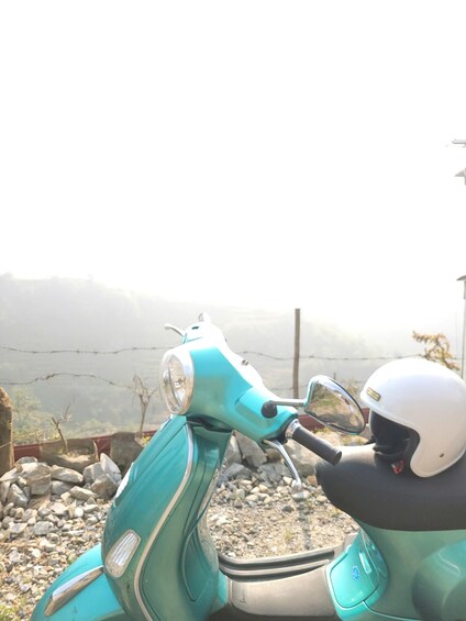 A teal scooter parked on a rocky surface with a person wearing a white helmet. 2