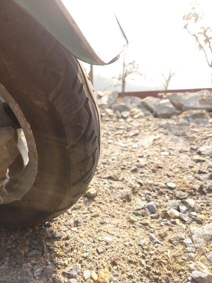 A close-up of a vehicle's tire on a gravel surface with sparse vegetation in the background. 1
