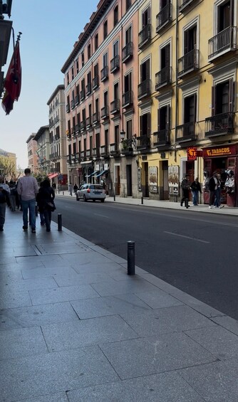 A street lined with multi-story buildings, pedestrians, and a parked car. 5