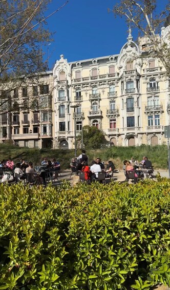 A group of people sitting at outdoor tables in front of a historic building with ornate balconies. 3