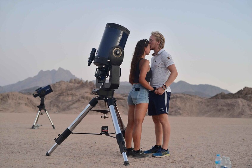 A couple standing in a desert with telescopes. 1