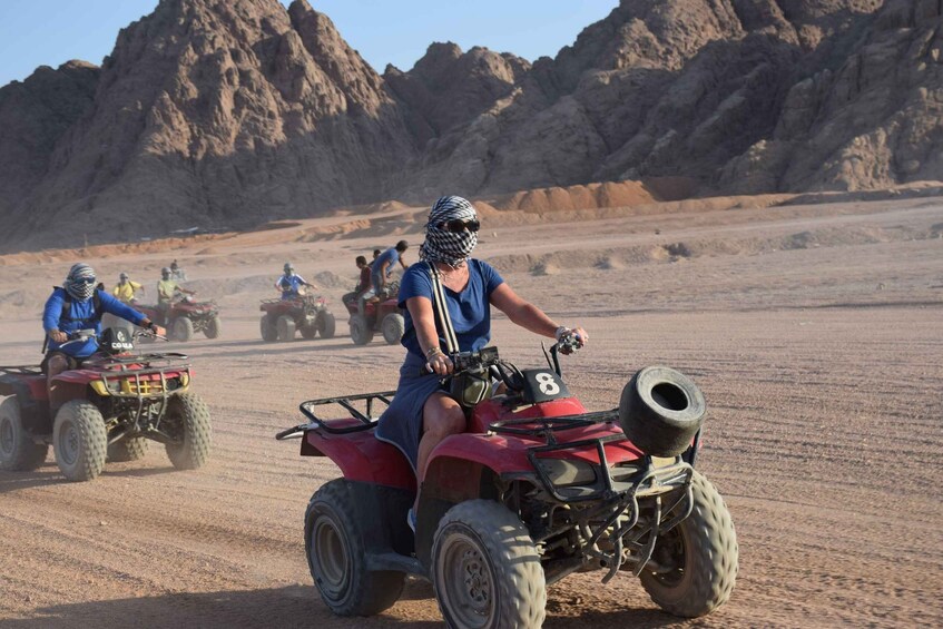 A group of people riding ATVs on a dusty trail with rocky mountains in the background. 5