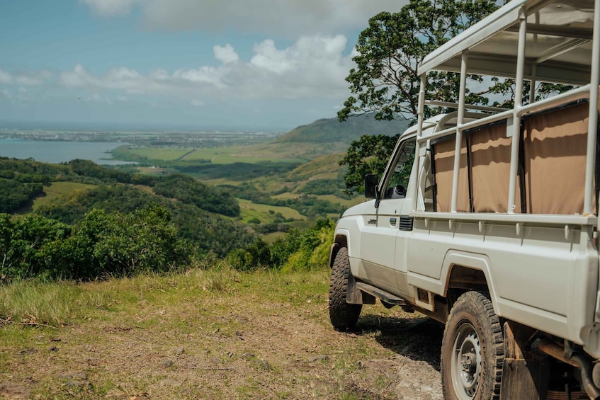 A white off-road vehicle parked on a grassy hill overlooking a valley with a body of water and distant buildings. 2