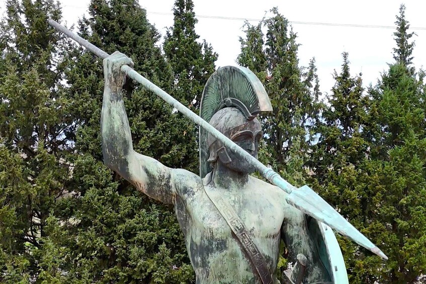 A statue of a warrior holding a spear, set against a backdrop of trees. 1