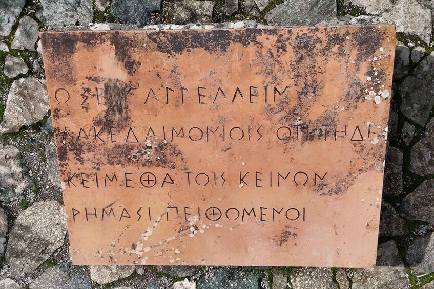 A weathered sign with Greek text on a rocky surface. 5