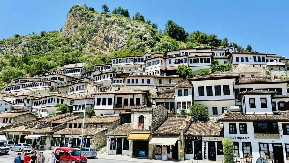 A hillside village with terraced buildings, a restaurant, and a mountain in the background. 1