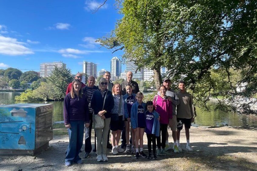 A group of people standing outdoors with a lake and buildings in the background. 3