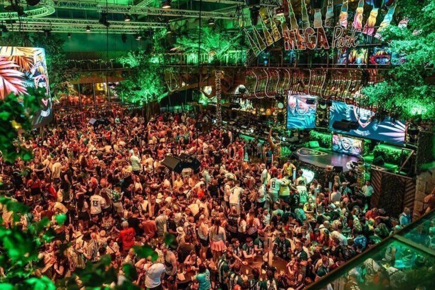 A crowded indoor venue with neon signs and a large screen displaying a game. 2