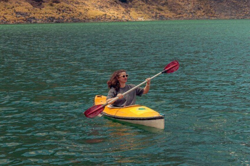 A person kayaking on a calm lake with a rocky shoreline in the background. 4