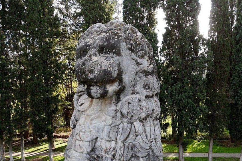 A stone lion statue in a park with trees in the background. 3