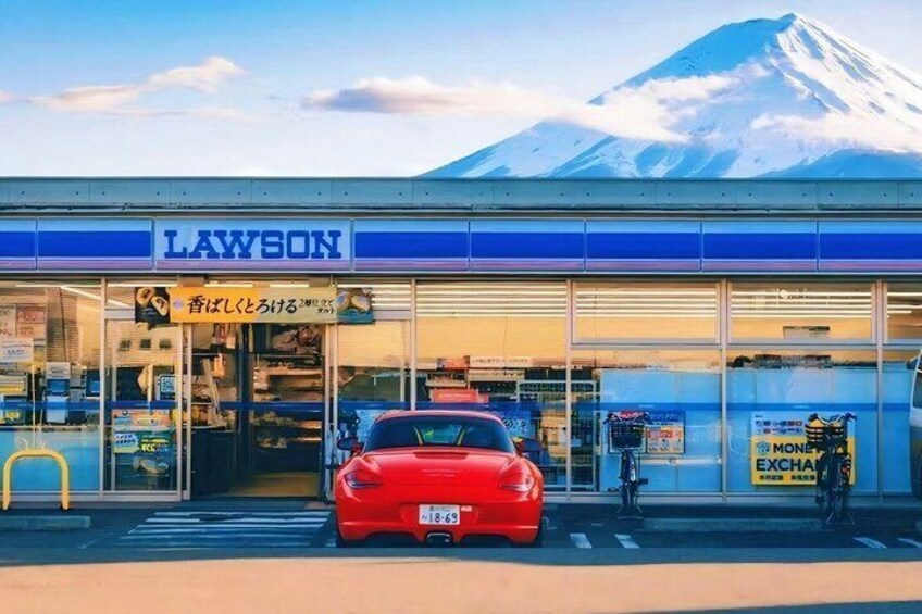 A Lawson convenience store with a red car parked in front, a mountain in the background, and a sign advertising a MONET EXCHANGE. 5