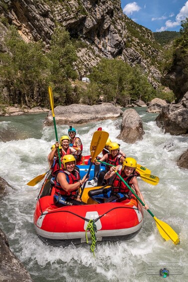 A group of people in a red inflatable raft navigating a river surrounded by rocky cliffs. 1