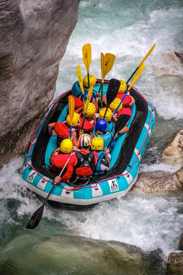 A group of people in a blue and white inflatable raft navigating a river with rapids. 5