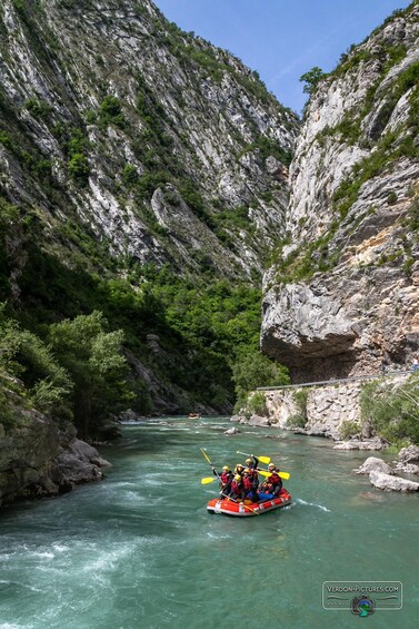 A group of people rafting down a narrow river surrounded by rocky cliffs. 2