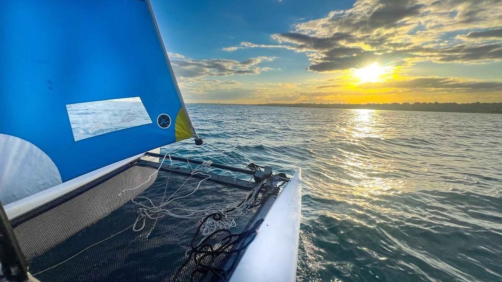 A sailboat with a blue hull and a white sail, sailing on calm waters during sunset. 1