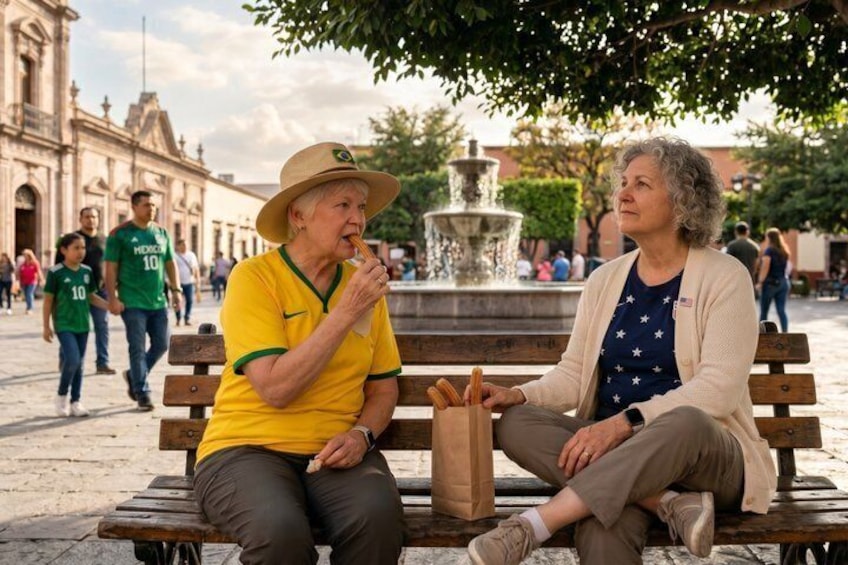 Two people sitting on a bench in a public square with a fountain and historic buildings in the background. 4