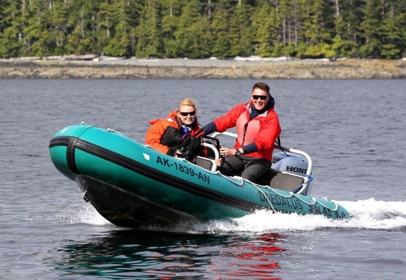 Two people in a green inflatable boat on water with a forested shoreline in the background. 3
