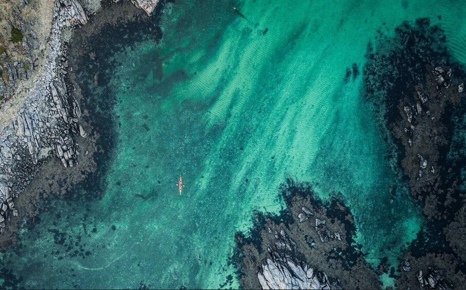 A kayaker in turquoise waters with rocky coastlines. 2