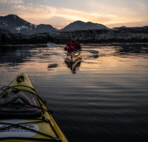 A kayaker in a red jacket paddling a kayak on calm water with mountains in the background. 3