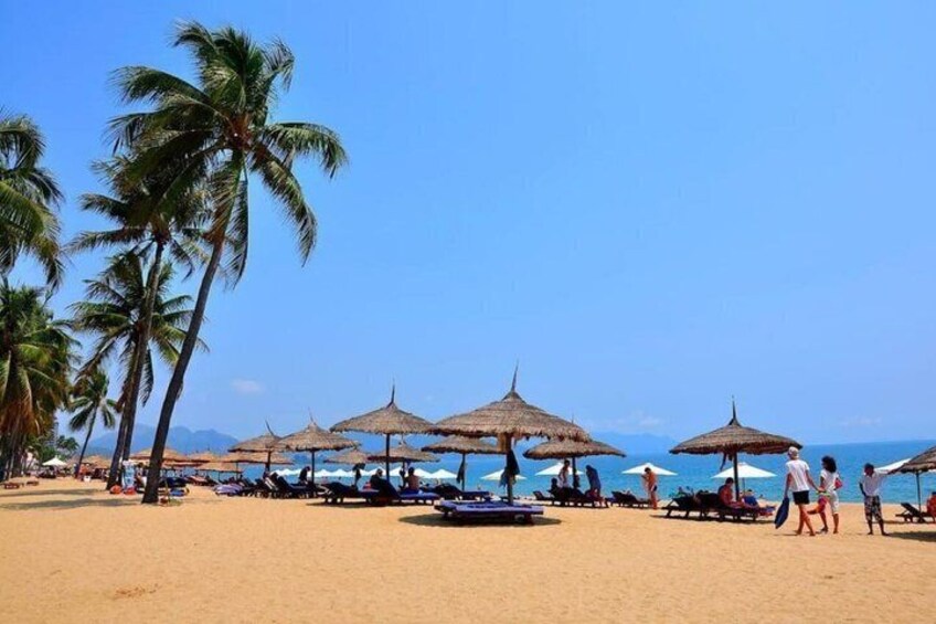 A beach with palm trees, beach umbrellas, and people sunbathing. 4