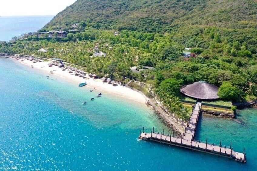 A coastal beach with a pier extending into turquoise waters, surrounded by lush greenery and a mountainous backdrop. 5