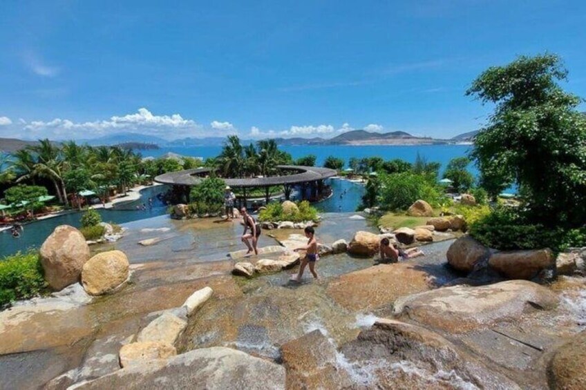 A natural hot spring with large rocks, a pool, and a building in the background. 1