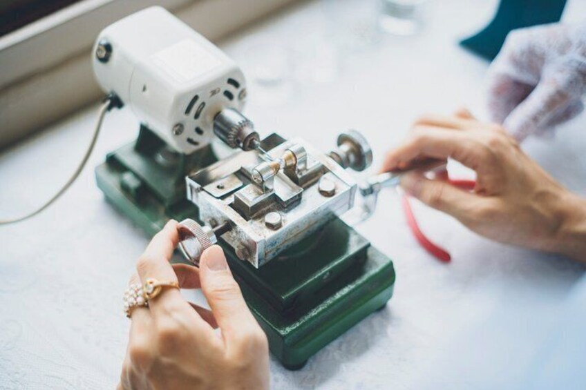 A person using a sewing machine, adjusting a metal plate, and holding a red tool. 5