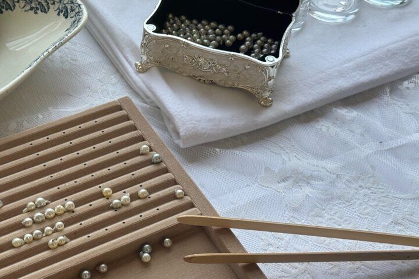 A wooden bead tray, a small metal container with beads, and a pair of wooden tongs on a white cloth. 1