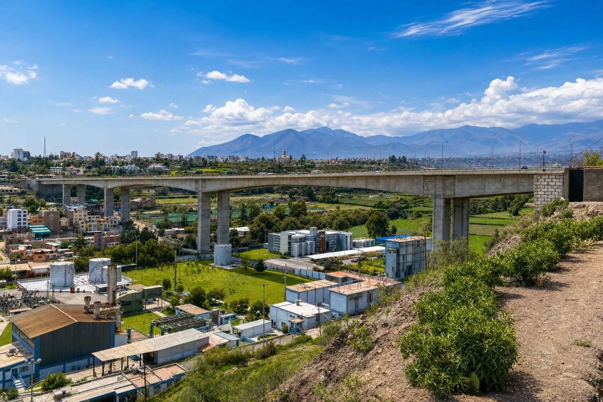 A bridge over a river, industrial buildings, and mountains in the background. 3