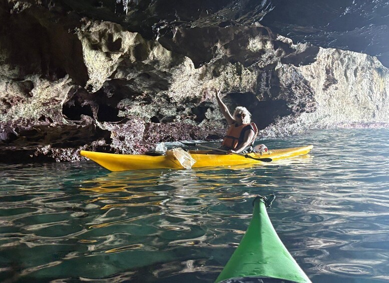 A person kayaking in clear water with a rocky cave background. 4