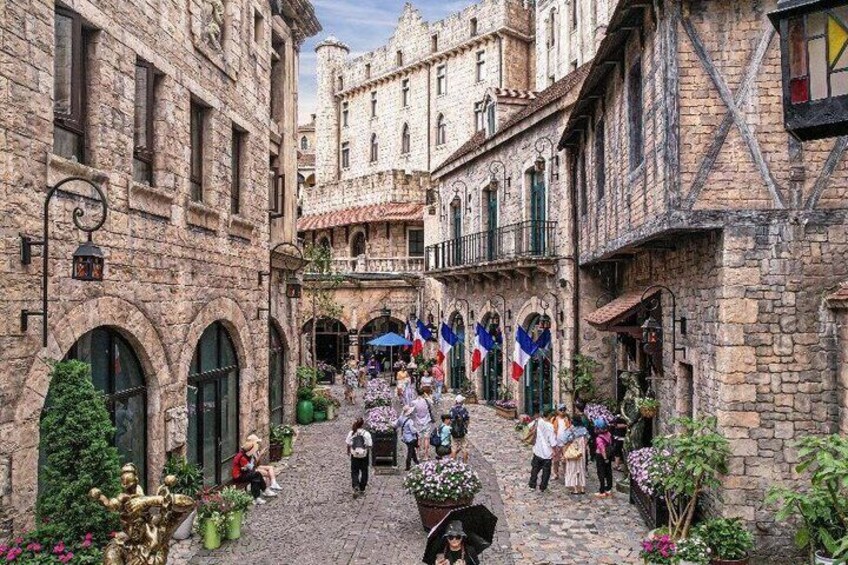 A cobblestone street with historic buildings, flags, and people walking. 2