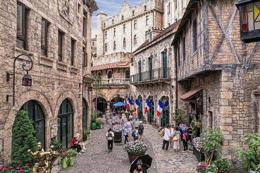 A cobblestone street with historic stone buildings, flags, and people walking. 4