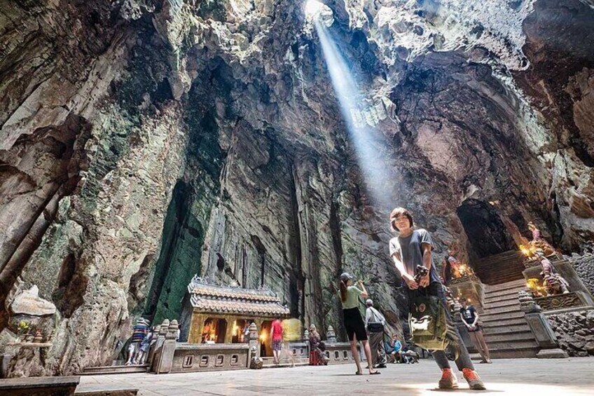 A cave temple with a small shrine, people visiting, and a person taking a photo. 5