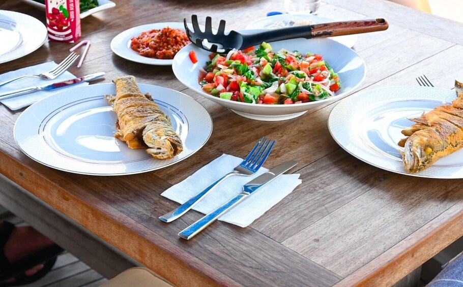 A wooden table with plates of fried fish, a bowl of salad, and a bottle of sauce. 3