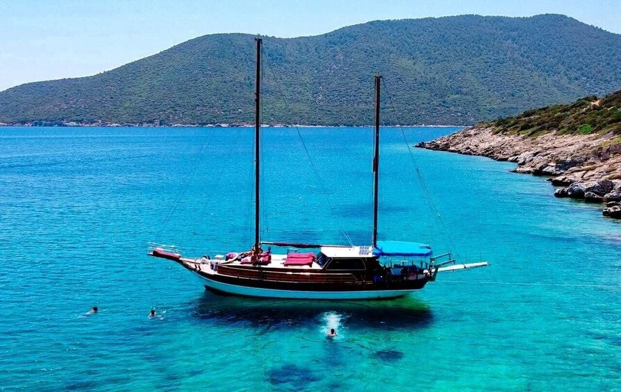A boat anchored in clear turquoise waters with a mountainous backdrop. 1